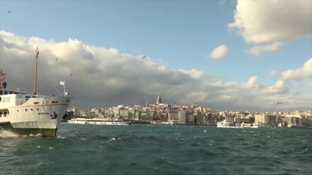 Галата башня, на переднем плане удовольствие лодки с туристами и чаек. Лодки удовольствия на фоне Галатской башни, ветреная погода — стоковое видео