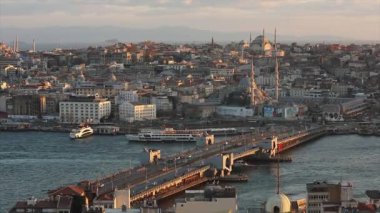 Gün batımında Galata Köprüsü ve camilerin manzarası. Bir sürü martı uçuyor, turist tekneleri yüzüyor.