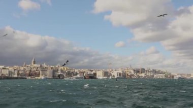Galata Kulesi 'nin ön planda turistler ve martılarla dolu eğlence teknelerinin çekimi. Galata Kulesi 'nin arka planında tekneler, rüzgarlı hava
