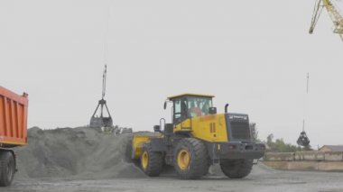 Limanda bir kamyon, iskele vinçleri, kazıcı kamyondaki malzemelere yükleniyor.