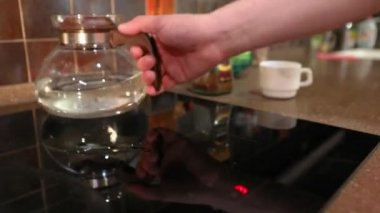 Adam çaydanlığı ocağa koyuyor. Tencere dibin kara seninki benden kara. Sobanın üzerinde cam çaydanlık.