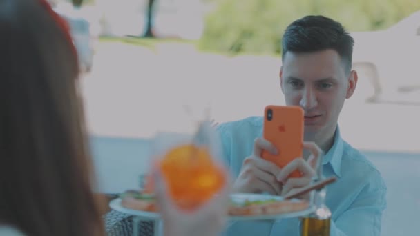 Chlap fotí holku u stolu v restauraci. Chlap fotí holku na smartphonu — Stock video