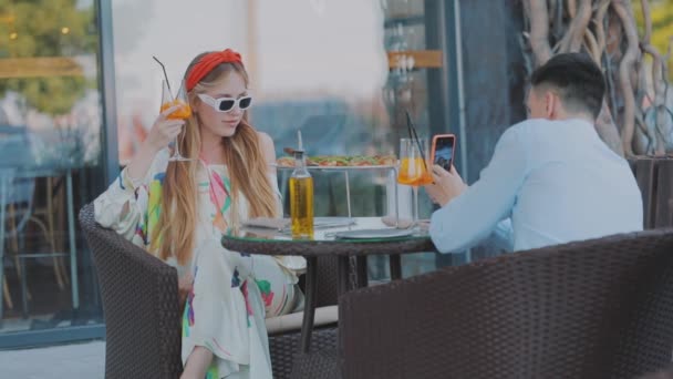 Um tipo fotografa uma rapariga numa mesa num restaurante. Cara fotografa uma menina em um smartphone — Vídeo de Stock