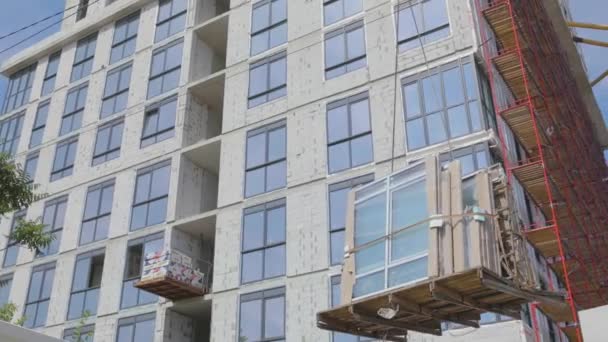 Werken in de thuisbouw. De kraan tilt dubbele beglazing op. Een kraan hijst ramen voor installatie in een woongebouw. — Stockvideo