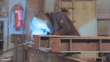 . Kaynakçı fabrikada çalışıyor. Kaynakçı metal bir parça metal kaynak makinesi topluyor.