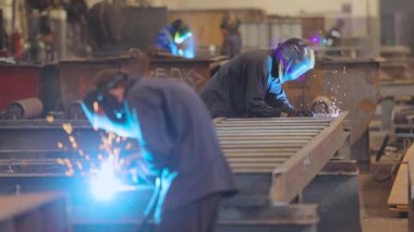 İki kaynakçı bir metal parçasını kaynaklıyor. Fabrikada metal bir yapıyı kaynak yapmak.