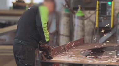 Adam bir atölyede öğütücü olarak çalışıyor, öğütücüden parlak kıvılcımlar çıkıyor.