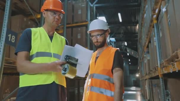 Dois engenheiros num armazém moderno. Duas pessoas no armazém estão a discutir algo.. — Vídeo de Stock