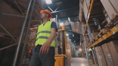 Elektrikli forklifti olan bir işçi. Depoda işçi forklifti var. İşçi depoda yürüyor.