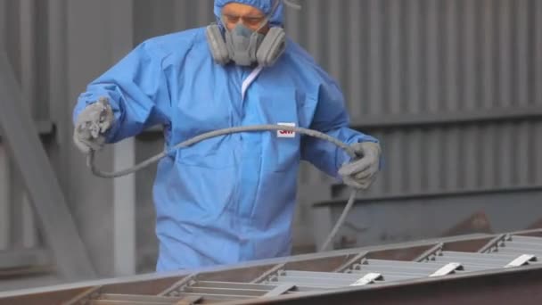 Een man in een beschermend pak schildert een groot deel, een spuitpistool, schildert een groot metalen deel — Stockvideo