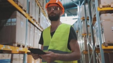 Büyük bir fabrikanın depo müdürü. Bir depoda elinde tablet olan bir müdür malları kontrol ediyor.