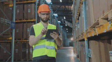 Büyük bir fabrikanın depo müdürü. Bir depoda elinde tablet olan bir müdür malları kontrol ediyor.