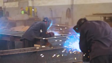 . Kaynakçı fabrikada çalışıyor. Kaynakçı metal bir parça metal kaynak makinesi topluyor.