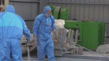Koruyucu takım elbiseli işçiler metal bir parça boyuyorlar. Fabrikada yarı boya.