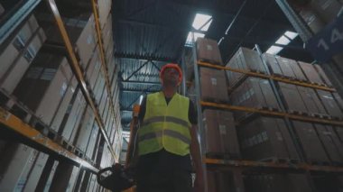 Bir işçi hidrolik forklift ile ağır çekimde yük taşır. Büyük, modern bir depo. Stokta modern özel ekipman