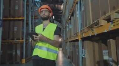 Büyük bir fabrikanın depo müdürü. Bir depoda elinde tablet olan bir müdür malları kontrol ediyor.