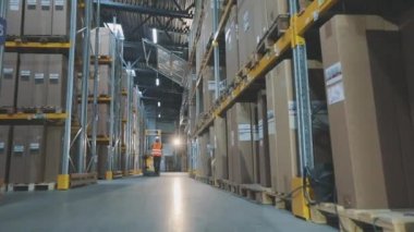 Büyük, modern bir depo. Bir işçi hidrolik forkliftle yük taşır. Stokta modern özel ekipman.