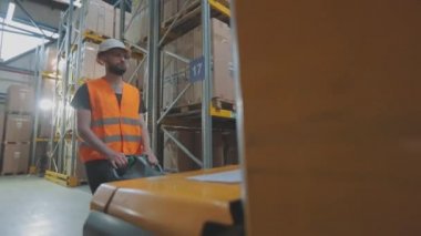 Depoda çalışan bir işçi elektrikli forklift taşır. Depoda forklift kullanan bir işçi. İşçi depoda yürüyor.