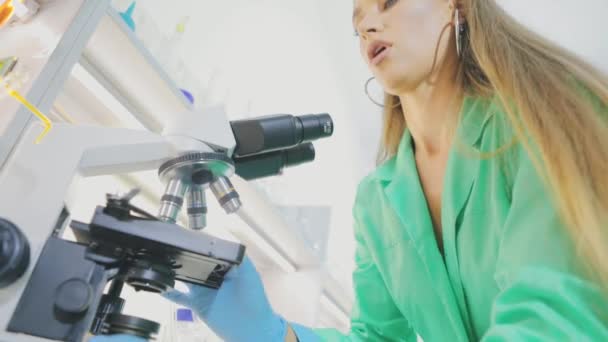 Девочка-вирусолог смотрит в микроскоп. Девушка-исследователь смотрит в микросому. — стоковое видео