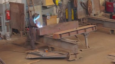 Fabrikada çalışan bir işçi metal bir yapıya kaynak yapar. Fabrika kaynakçısı