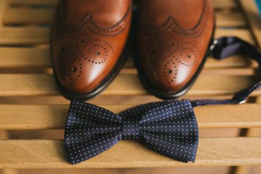 A pair of brown stylish leather men's brogues shoes beside a bow tie. Accessories for the groom clipart