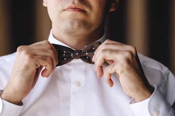Beyaz bir gömlek damat erkekte kahverengi papyon elleriyle düzeltiyor. Yakın çekim