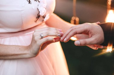 Düğün töreni. Pembe elbiseli gelin damat için bir parmağına bir nişan yüzüğü takıyor. Elinde bir elmas yakın çekim ile altın bir yüzük var. Yatay