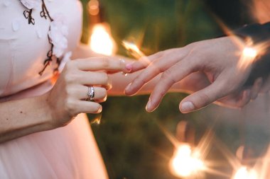 Düğün töreni. Pembe elbiseli gelin damat için bir nişan yüzüğü ampulleri bokeh arka plan üzerinde giyiyor. Elinde bir elmas yakın çekim ile altın bir yüzük olduğunu.