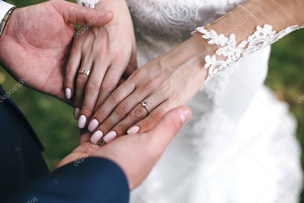 The groom holds the bride's hands with a beautiful manicure and engagement ring with precious stone. Horizontal