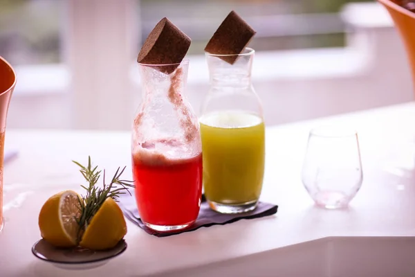 Two bottles with lemonade (mint and forest fruits), an empty dirty glass and a sliced lemon with rosemary on a bar