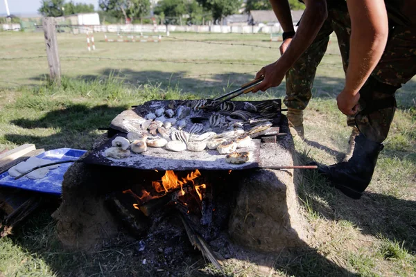 Soldiers preparing meal on a handmade grill on open wooden fire, at a survival camp. They cook water snakes, fish, frogs and bread.