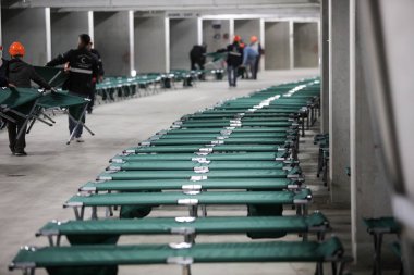 Camp folding cots are being set up in the underground parking of a stadium and wait for refugees, during the drill of a catastrophic earthquake in the city in which there are many victims clipart