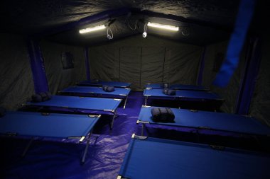 Camp folding cots and sleeping bags are being set up in tents and wait for refugees, during the drill of a catastrophic earthquake in the city in which there are many victims clipart