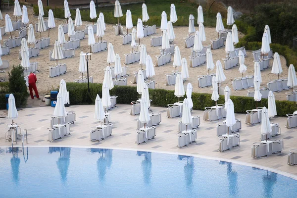 Closed sun umbrellas and lawn chairs around a hotel pool in off season, with no people in a cold cloudy day, in late autumn on the Bulgarian seaside