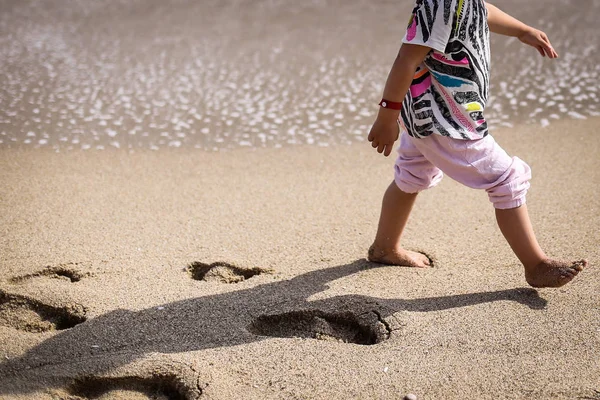 Lonely child walks on the beach leaving foot imprints in the sand