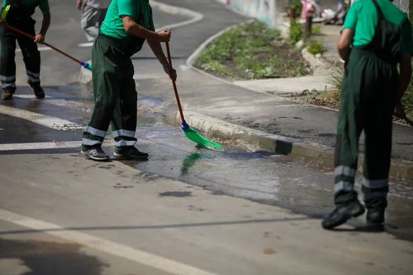 Barrendero limpieza de la acera de la ciudad con agua de una manguera y — Foto de Stock