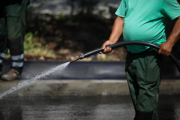 Man with big belly uses a hose to sprinkle water on the pavement