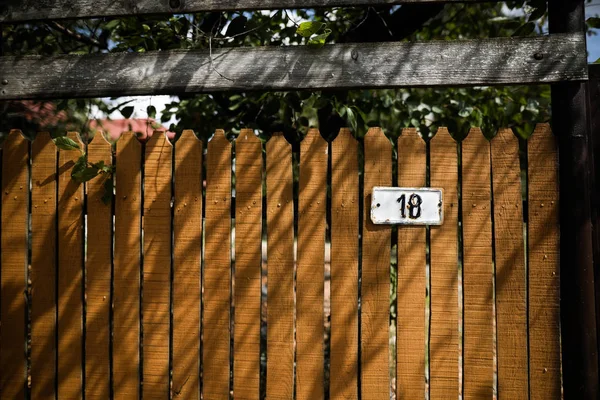Sarı ahşap çit üzerinde eski ve yıpranmış metal ev numarası — Stok fotoğraf