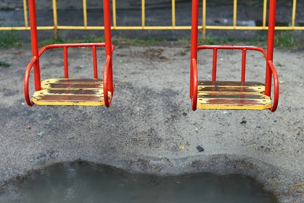 Metal swing with a wooden seat on a kids playground on a rainy day with a puddle under it