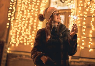 Güzel genç kadın kürk paltolu bir maytap holding eski karlı Avrupa şehri şenlikli sarı ışık bokeh arka plan üzerinde kış Noel havasında sahiptir