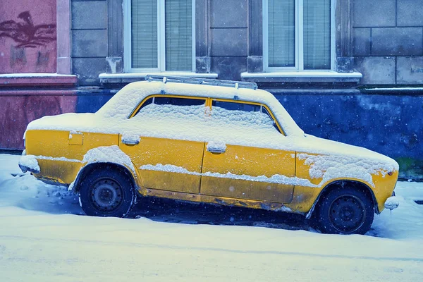Старий жовтий автомобіль вкритий снігом, припаркований на сніговій похилій вулиці в зимовому місті — стокове фото