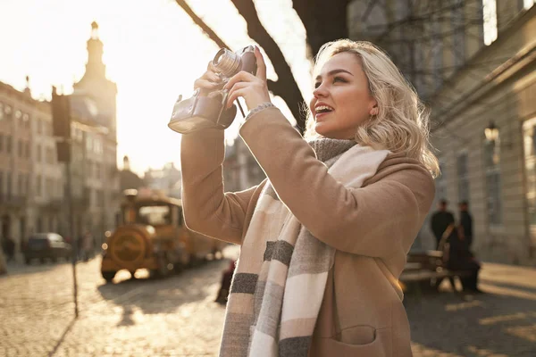 Junge schöne, fröhliche blonde Frau beim Fotografieren mit ihrer Filmkamera an einem sonnigen Tag auf dem Rynok-Platz in Lwiw, Ukraine — Stockfoto