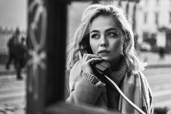 Jovem mulher loira bonita fazendo uma chamada importante em uma cabine telefônica pública vintage em uma noite ensolarada — Fotografia de Stock