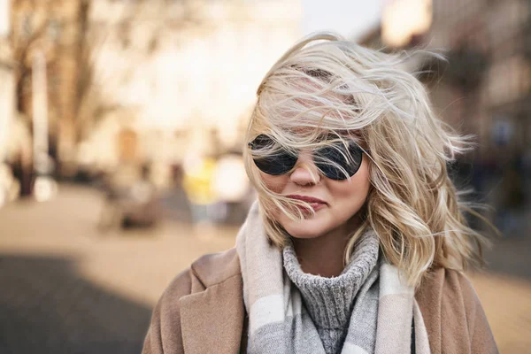 Der Wind bläst ihr blondes Haar zu und bedeckt ihr Gesicht und ihre Sonnenbrille — Stockfoto