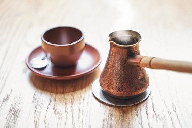 Oryantal Türk tarzında buharlı sıcak kahve, ahşap bir masanın üzerine dökülen dudak ve fincan ile küçük uzun saplı bir tencere cezve servis
