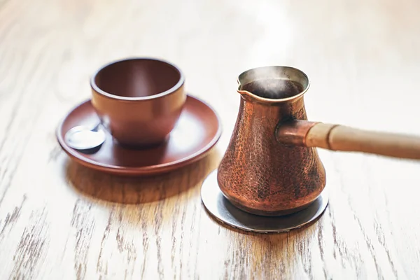 Oryantal Türk tarzında buharlı sıcak kahve, ahşap bir masanın üzerine dökülen dudak ve fincan ile küçük uzun saplı bir tencere cezve servis — Stok fotoğraf