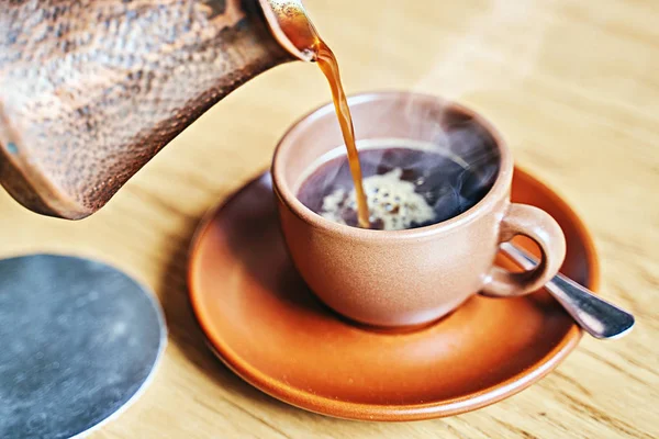 Café caliente con vapor en estilo turco oriental servido en cezve, una pequeña olla de mango largo con un labio verter y taza sobre una mesa de madera —  Fotos de Stock