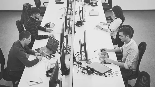 Молодые специалисты работают в современном офисе. Группа разработчиков или программистов, сидящих за рабочими столами, сосредоточилась на компьютерах в открытом пространстве ИТ-компании. Команда за работой. Высокое качество изображения . — стоковое фото
