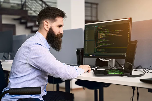 Software programmering. Bebaarde man werkt op computer in IT-kantoor, zittend op Bureau schrijven code, werken aan een project in software development bedrijf of Startup. Beeld van hoge kwaliteit. — Stockfoto