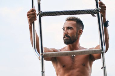 Genç, yakışıklı Müslüman kaptan yatına bir tekne merdiveniyle tırmanıyor ve denize bakıyor.